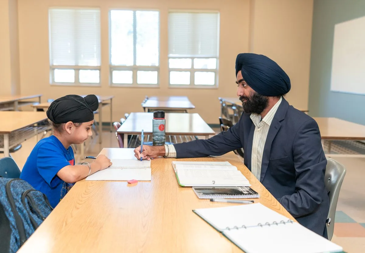 Indian teacher guiding a student at a classroom desk